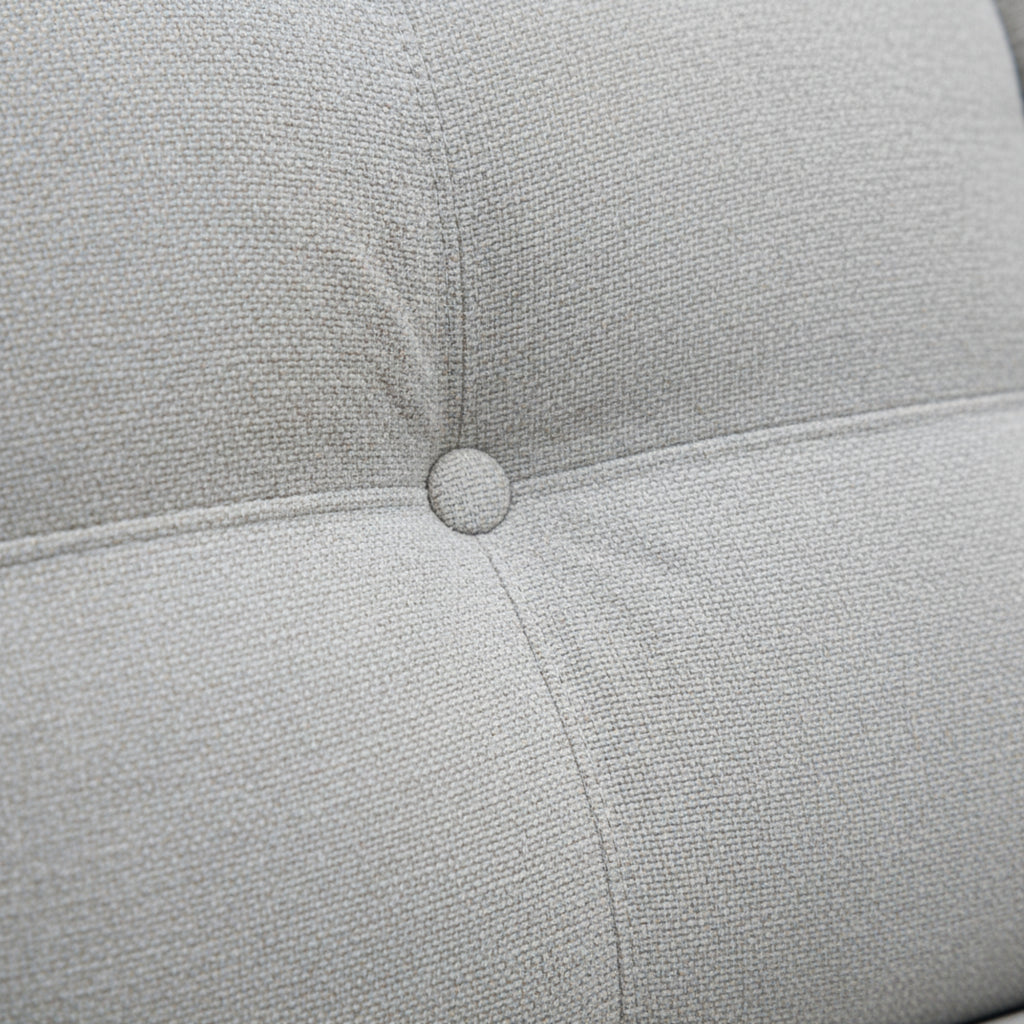 Close-up of a light gray cushion with a button on a textured fabric background