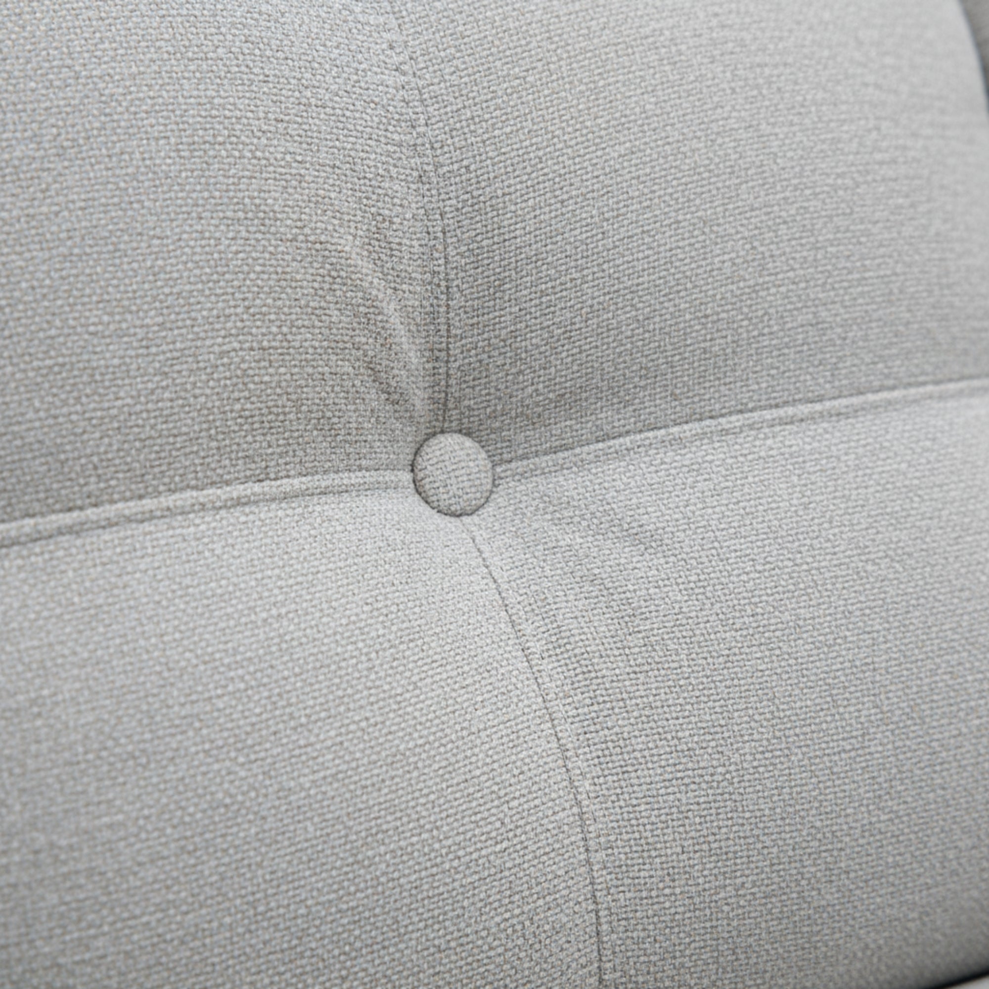 Close-up of a light gray cushion with a button on a textured fabric background