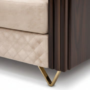 Close-up of a beige quilted sofa with a brown wooden side table and gold metal leg.
