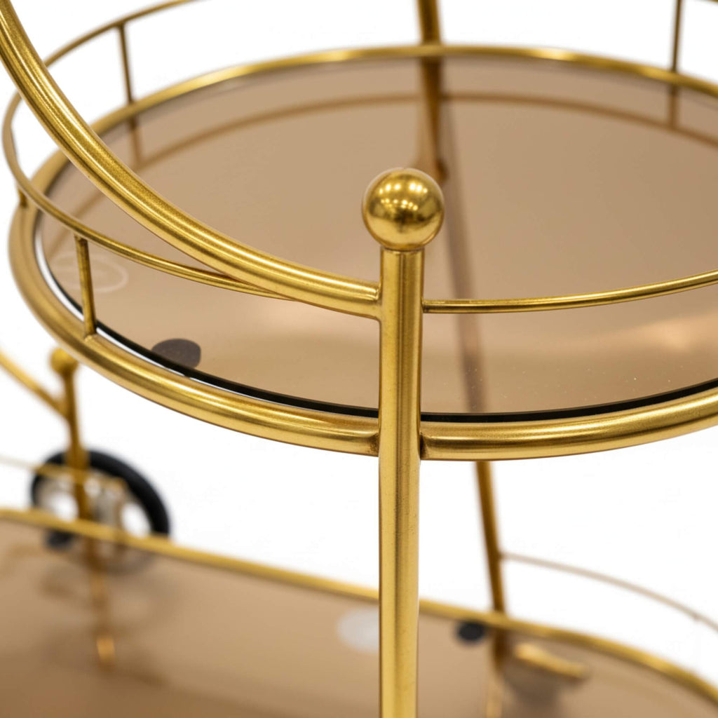 Gold metal bar cart with glass shelves on a white background