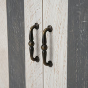 Close-up of a wooden cabinet with two bronze handles on a striped background.